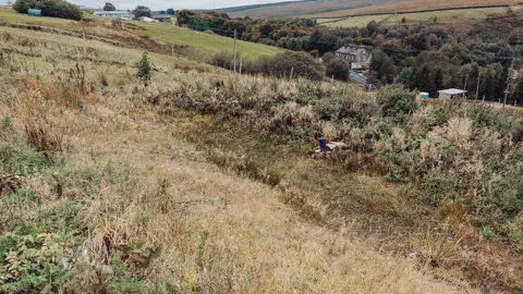 A dry pond known as an attenuation basin on the hillside at Annabut Lee Farm above Cragg Vale, that fills during heavy rainfall.