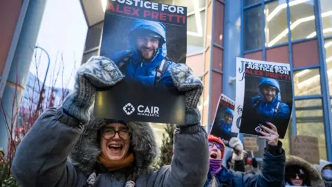 People shout and wear warm coats and hats as they hold up photos of Alex Pretti with signs reading 'justice for Alex Pretti' in Minnesota on Monday.