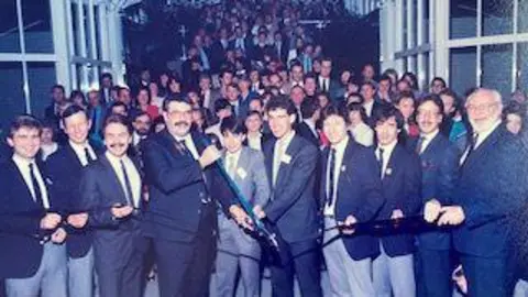Charles J. Wesoky A crowd of men in suits stand in front of a barrier they are about to cut with a huge pair of scisors 
