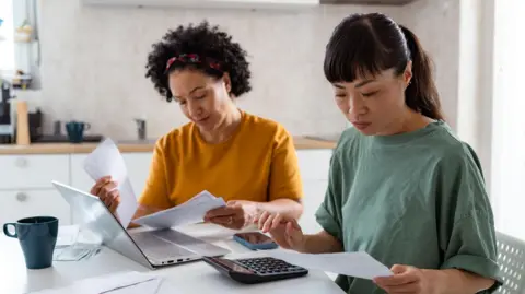 Two women looking at bills with a laptop and calculator on the table in front of them