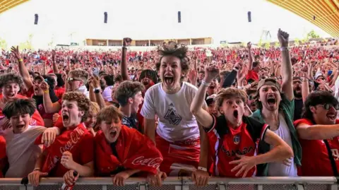 Reuters An image showing hundreds of fans jumping for joy after Canada scored a goal at the Fifa Fan Festival in Vancouver. Most are wearing read and white. They are gathered behind a metal railing. 