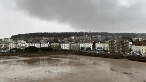 Cheryl/Weather Watchers A view of Weston-super-Mare's coast from the beach. Houses are set against a backdrop of a grey, stormy sky.