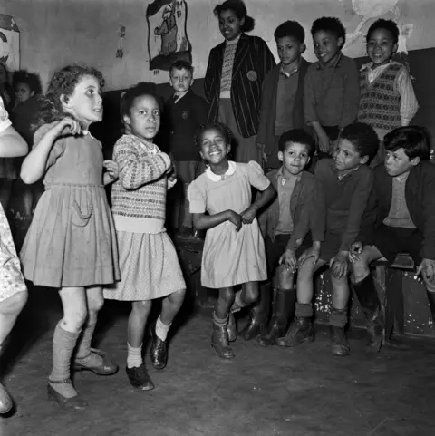 Bert Hardy/Getty Images Three young girls dance as others look on.