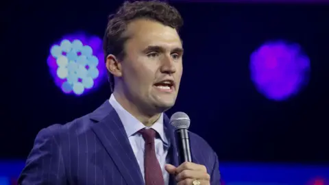 Getty Images Charlie Kirk wearing a tie and holding a microphone on a stage