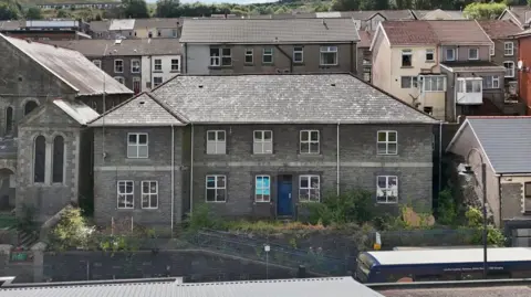 Paul Fish Auctions The exterior of the police station - a brick building with a slate roof and windows with white window frames. 