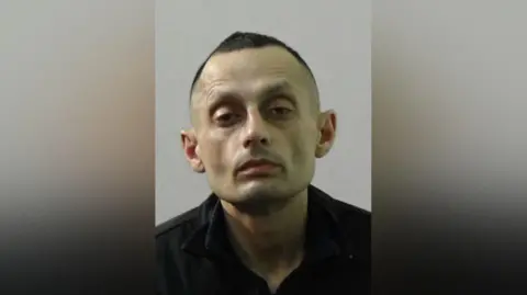 Northumbria Police Mugshot of Asim Kayani. He has a spaced out expression with his eyes partially closed, is clean shaven with short black hair and wearing a black top.