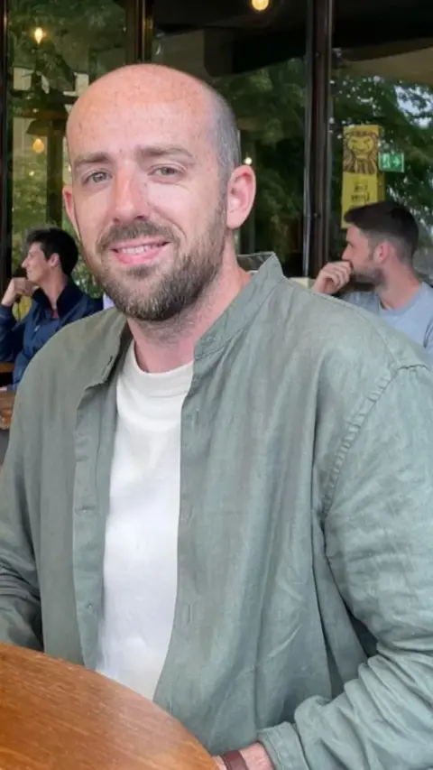 A man in a green shirt. He has no hair but has some stuble.