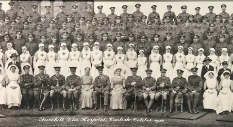 University of Cumbria A black and white image dated 1918 with six rows of soldiers and nurses posing for a photo outside the Skiddaw building in Carlisle. The men are all in military uniform, with the nurses wearing white nursing gowns and headwear, some with crosses stitched on their front.