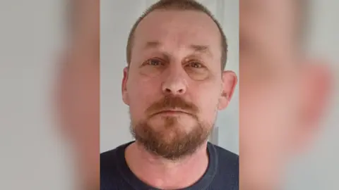 Provided A photo of Michael, who has very short hair, light-coloured eyes, and a ginger-brown goatee.