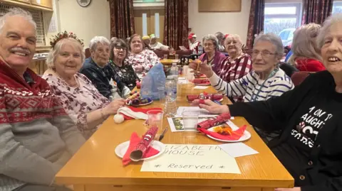 Swindon Borough Council A group of pensioners round a festive table in a care home, all smiling with crackers on plates in front of them.