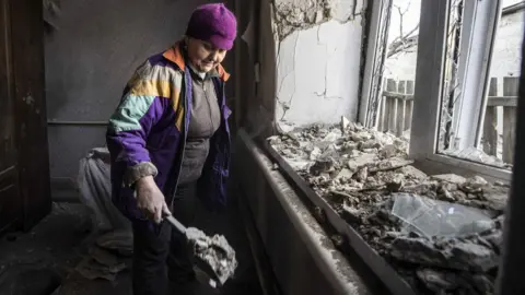 Anadolu Agency via Getty Images A woman cleans her damaged house after artillery fire from Donetsk region under the control of pro-Russian separatists in Donbas on February 23, 2022 in Mar'inka, Ukraine.