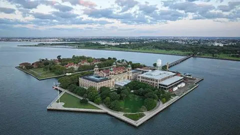 Getty Images Ellis Island shown from above: the island has a number of buildings, and is joined to the mainland by a bridge.  