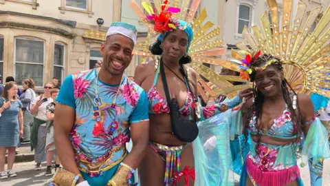 Three people dressed in colourful carnival costumes on a summer's day