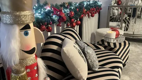 IWC Media Striped black-and-white chair with decorative pillows next to a garland of greenery with red ornaments on a bannister, with a large nutcracker figure in the foreground.