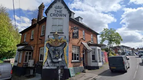 External shot of The Crown in Billericay. A mural of an animal wearing a crown is painted on one wall of the building, which sits on the corner of a road 