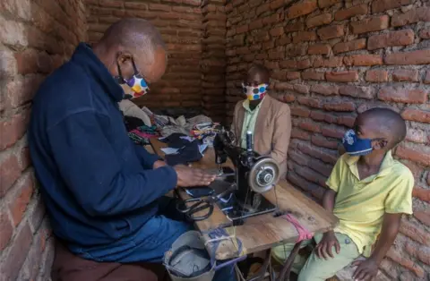 AFP Two masked people look on as a tailor creates face masks.