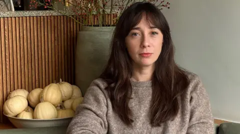 Katya Milavic-Davies A woman with long dark brown hair looks sadly at the camera