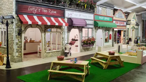 A mocked-up high street lined with shops and small picnic benches outside. Signs on the shops read "Lotty's Tea Room", "Hair and Beauty Salon", and "Post Office". There is also a cinema.
