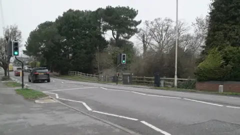 A picture of a pedestrian crossing on Herbert Avenue in Poole. There are white zig zag lines in the foreground, the traffic lights are showing green. There are a few cars in the distance.