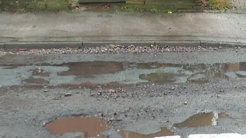 Many potholes in a road, filled with water