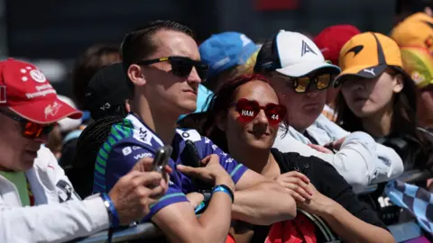 Reuters/Andrew Boyers General view of fans ahead of the British Grand Prix. They are leaning on a barrier, wearing dark glasses and baseball caps. 