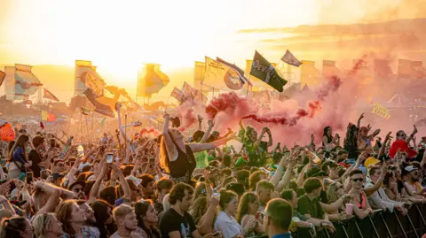 Ben Birchall/PA Media A crowd at Glastonbury Festival holding flags and flares