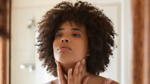 A woman, standing in front of a mirror, examining her eye wrinkles 