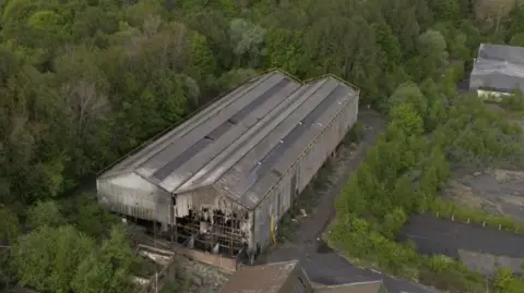 An aerial shot of the building where the fire took place. The front is damaged. It is surrounded by trees.