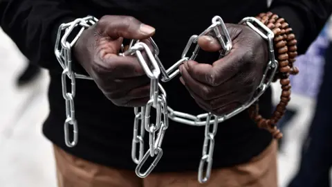 LOUISA GOULIAMAKI An African migrant with his hands chained, takes part in a march towards the offices of the European Union during a demonstration on December 2, 2017 in central Athens, protesting against the slavery of migrants in Libya.