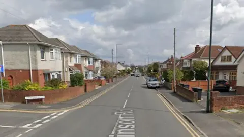 Kinson Road with homes lining both side and cars driving towards the camera. A junction can be seen on the right and then another further down on the left.