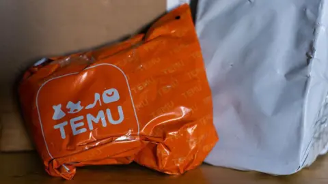 Getty Images An orange Temu parcel is pictured on a wooden floor with other parcels