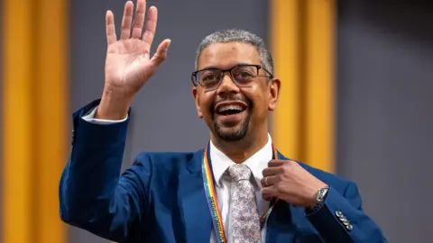 PA Media Vaughan Gething waves to the camera.