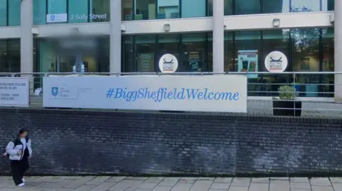 A low wall with railing and a banner saying #BigSheffWelcome sits in front of a modern glass building