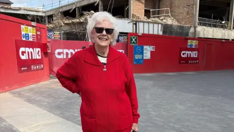 Kevin Shoesmith/BBC News A woman with curly short grey hair wears a grey cardigan. A building site is in the background.