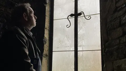 Mr McAleavy looks out through an old ornate window in a basement that would once have been part of the medieval abbey.