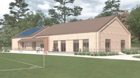 The proposed sports hub is made up in a graphic. It has a wooden design walls and a brown roof. Solar panels can be seen on one section of the roof. There is a sports pitch of some sort in front of the building too, just to the left of the picture.