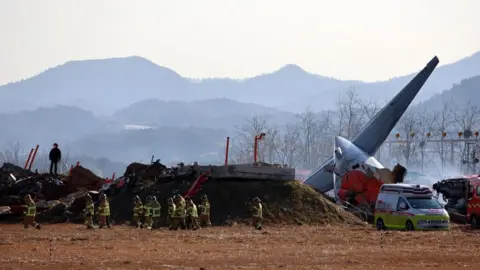 Firefighters walking next to a large piece of debris from the plane