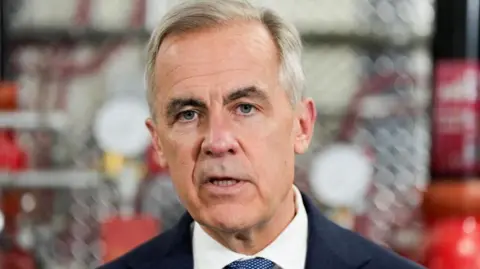 A close-up image of Mark Carney mid-speech. He has short grey and black hair and grey eyes. 