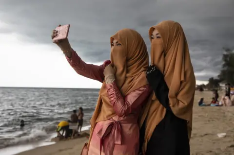 Paula Bronstein / Getty Images Thai women take a selfie on the Talo Kapo beach