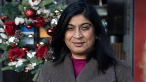 Facundo Arrizabalaga/My London Sital Punja is pictured standing outdoors in front of a Christmas wreath decorated with red and gold baubles, looking towards the camera.