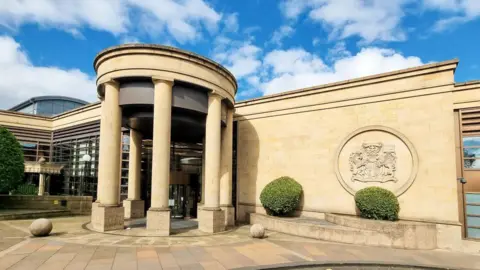 Exterior of High Court of Glasgow. A brown stone building with a round, pillared entrance and court of arms on the wall.