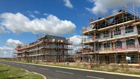 Shariqua Ahmed /BBC Exterior of  houses under construction with scaffolding in front 