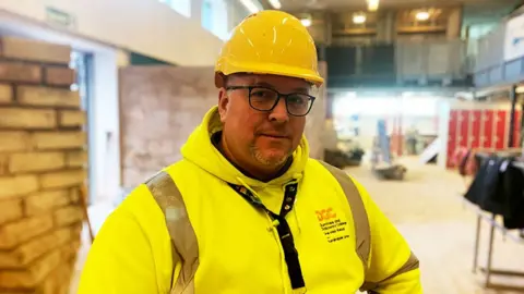 A man in a yellow top and a yellow hard hat with glasses and a beard