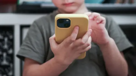 Close up of  a child holding yellow smartphone, he is wearing a grey t-shirt.