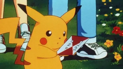 PA Media An image of a yellow Pokémon character with long pointed ears and red cheeks. it is holding a piece of paper.