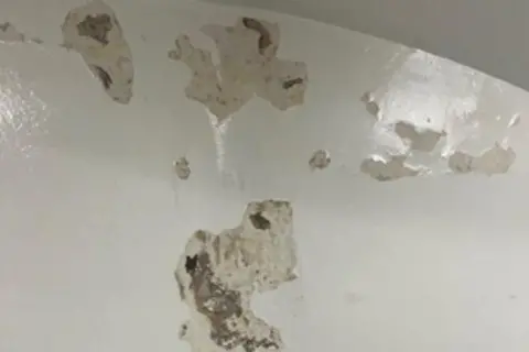HMIPS Chipped and broken plaster on the white wall of a cell in a custody unit
