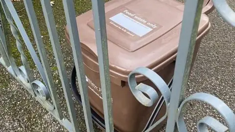 New Forest District Council A brown New Forest District Council food bin on the ground behind a closed metal gate