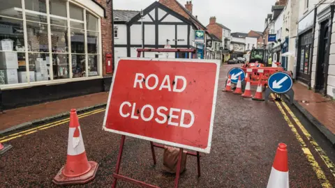 Getty Images A Road Closed Sign With Traffic Cones And Construction Barriers Blocking A Street In The Background - stock photo