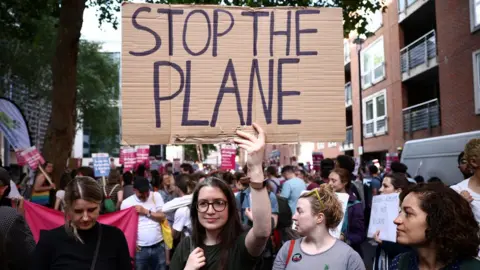 Reuters A woman in a crowd holds a sign saying 'stop the plane'
