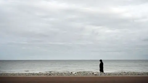 Getty Images person walking along empty beach